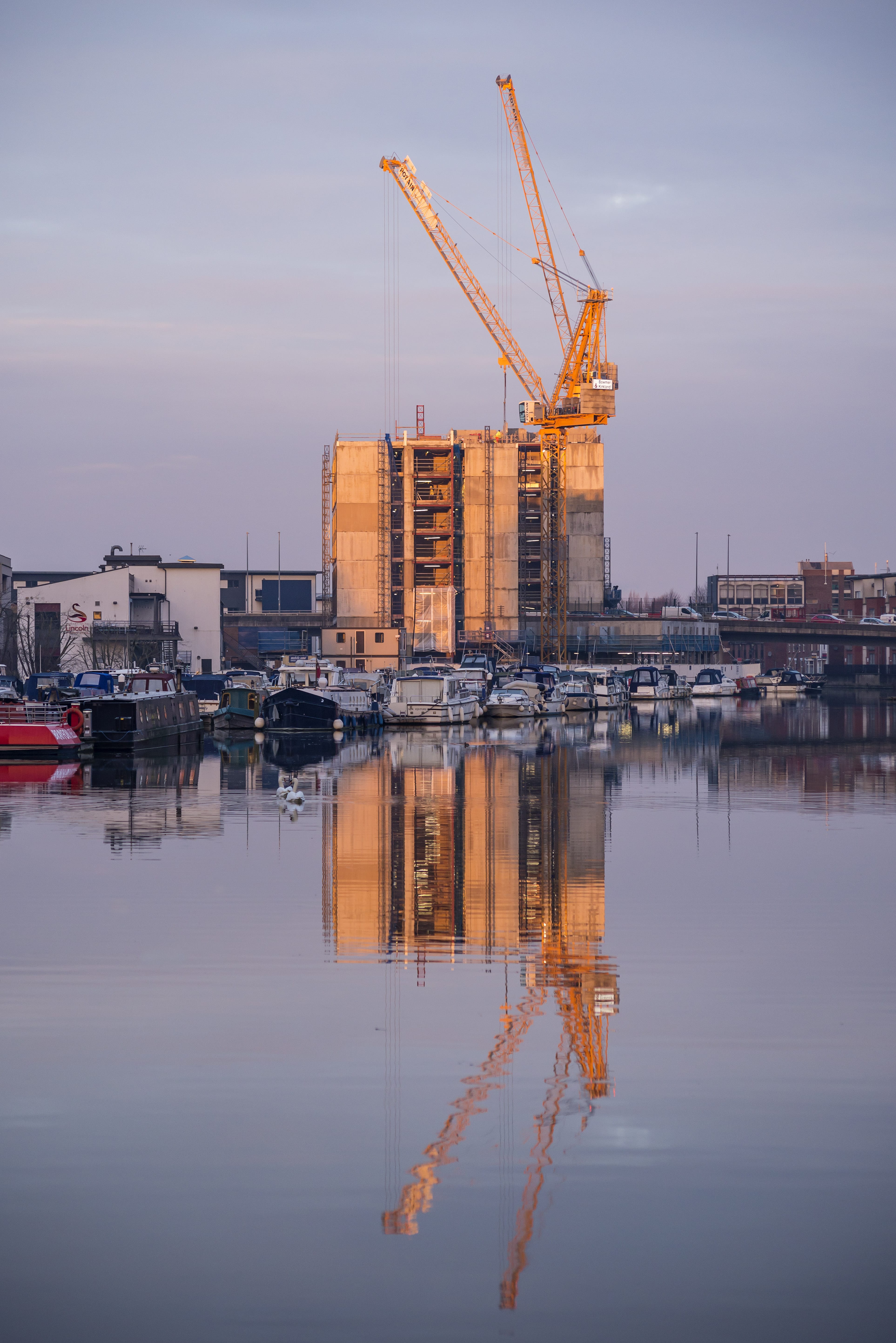 Image of an accommodation block being built by the water, a crane towers above it.