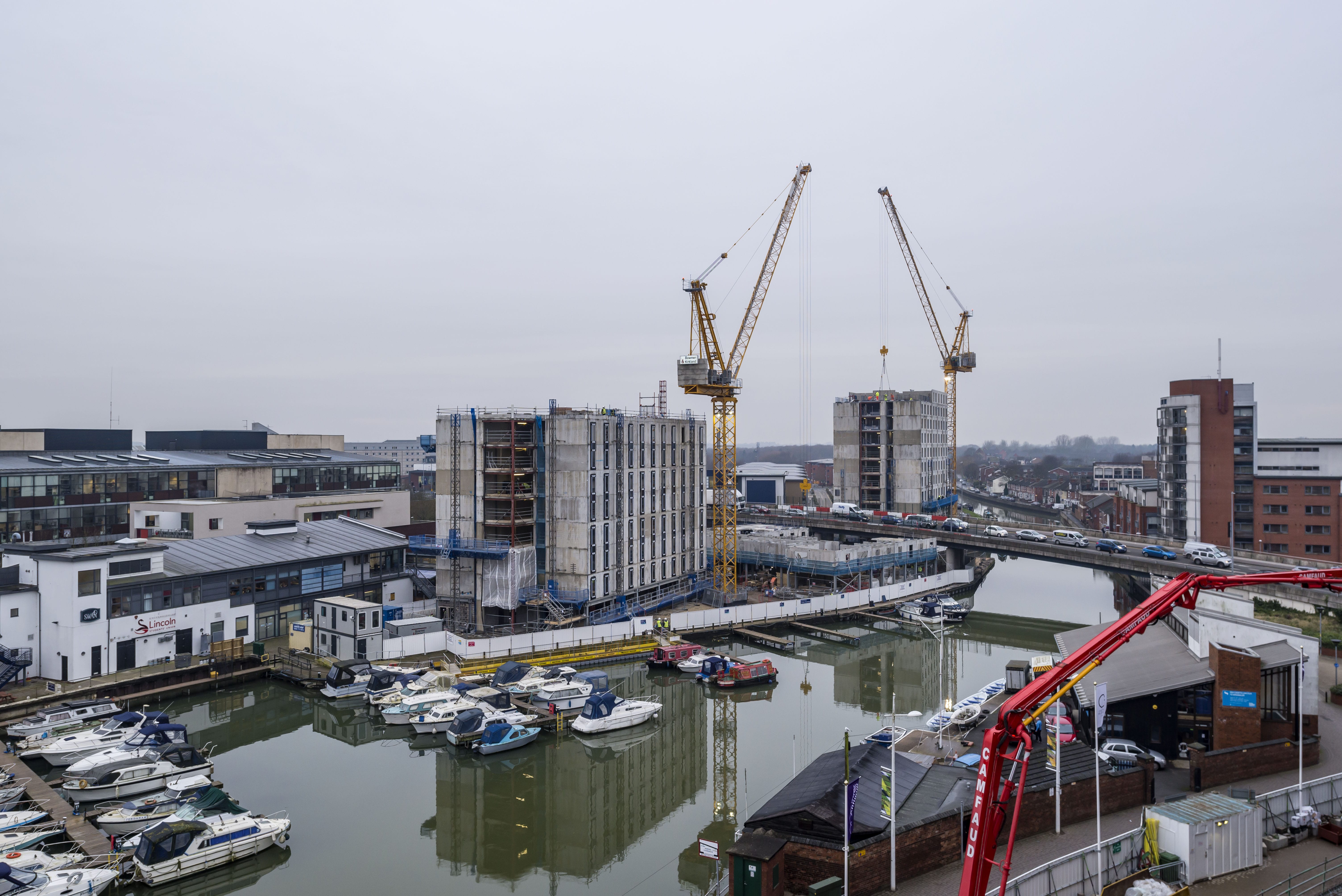 Image of the an accommodation block being built, two cranes work across a flyover