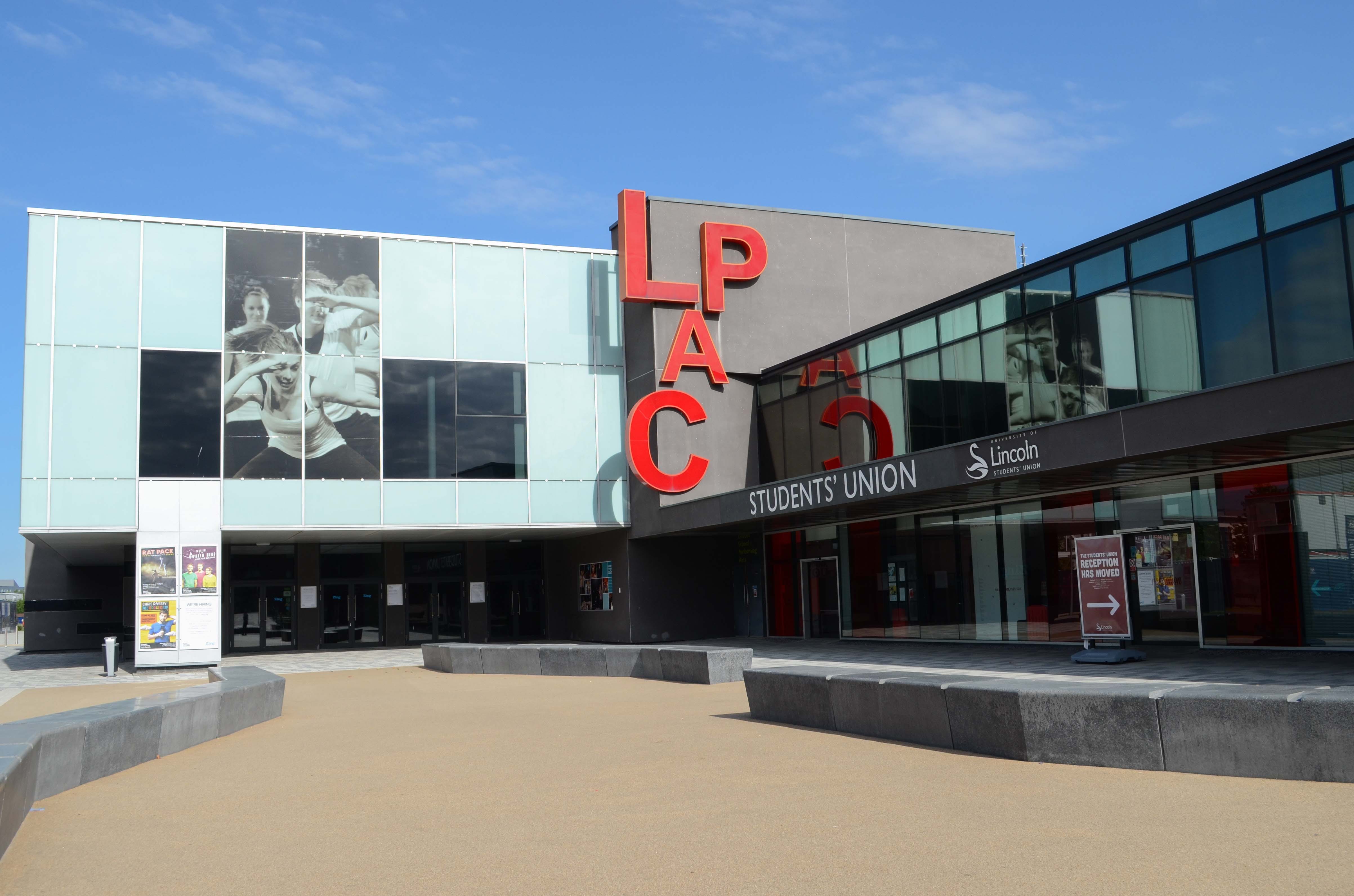 Image of a theatre, a large light blue and grey building with "LPAC" signage in red