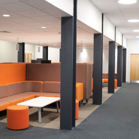 Image of a social learning space, including orange sofas and white tables. The furniture has inbuilt power.