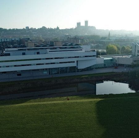 Image of the Brayford campus buildings, there is the delph pond in the foreground and the cathedral on the horizon