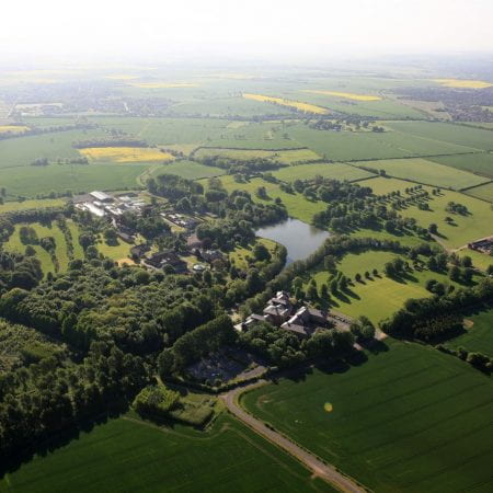 Aerial image of a green university campus with fields and woodlands surrounding it