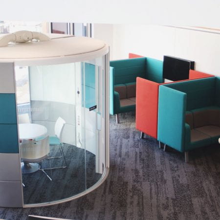 Image of booth chairs and small tables. There is a small office pod with a table and chairs in it also