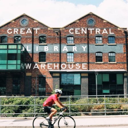 Image of a red brick library building, a cyclist is cycling past it