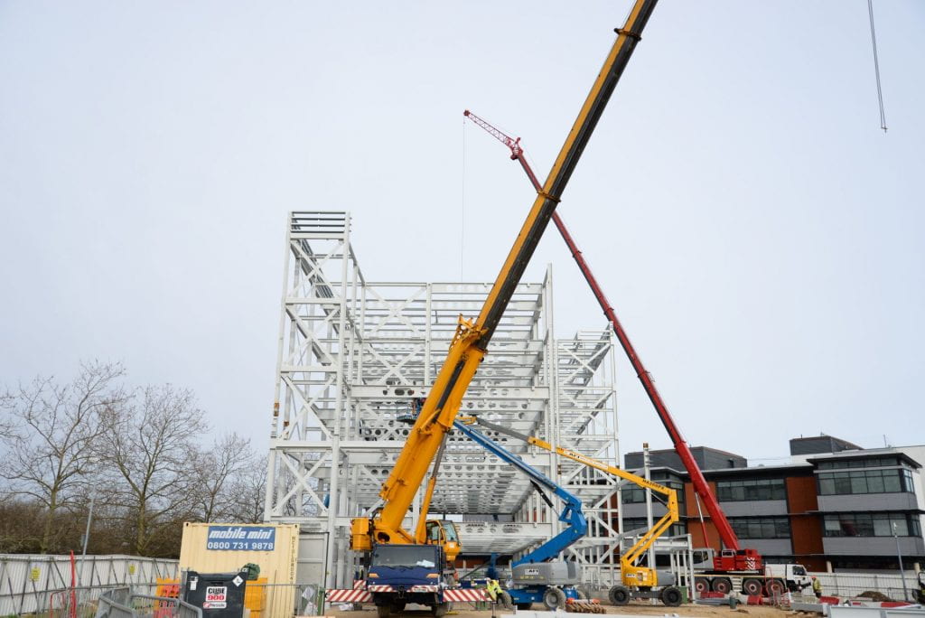 Image of a steel frame of a building with diggers infront