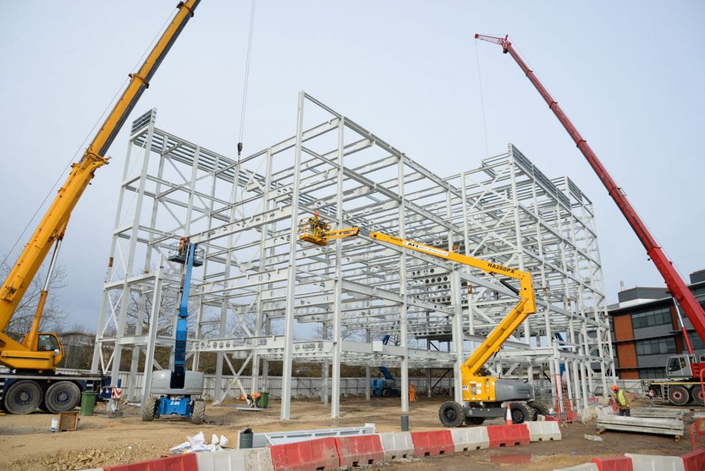 Image of a steel frame of a building with diggers infront