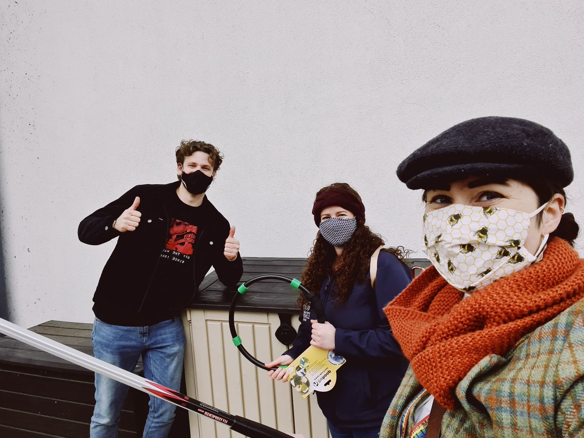 Three people hold litter picking equipment and look happy under their masks. They are socially distanced.