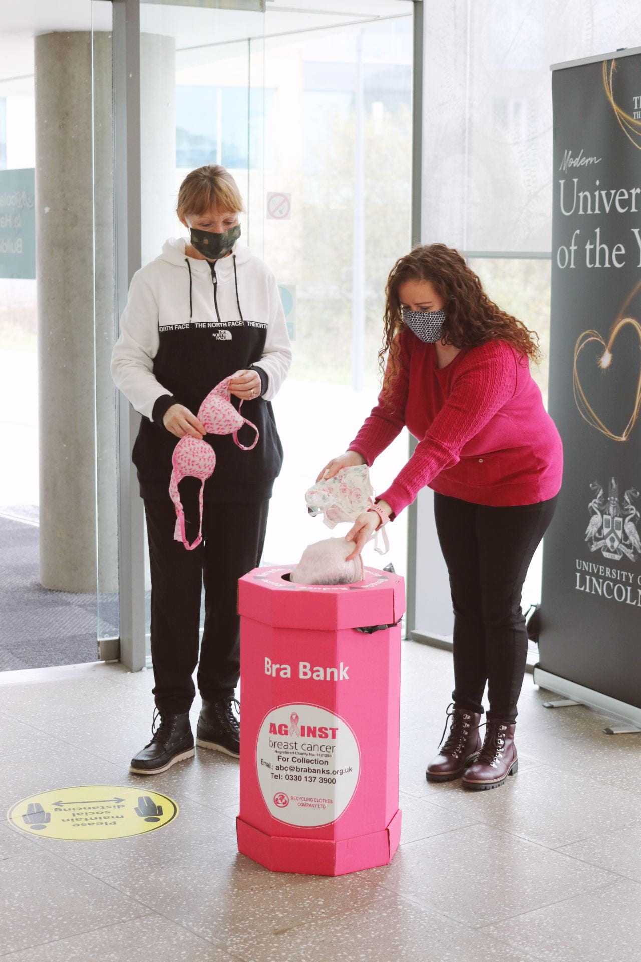 Image of two people putting bras into a pink recycling bin