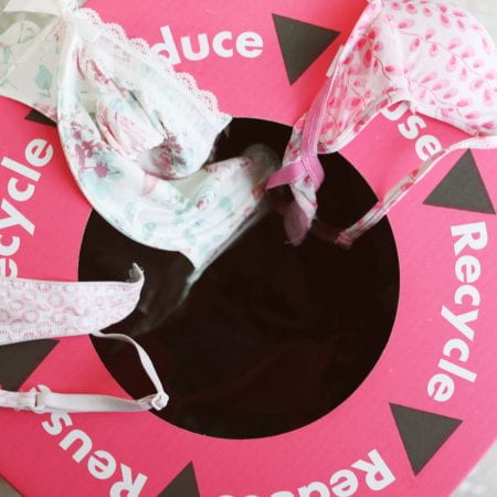 Image of a pink recycling bin with bras on top of it. The word recycle is printed on the lid.