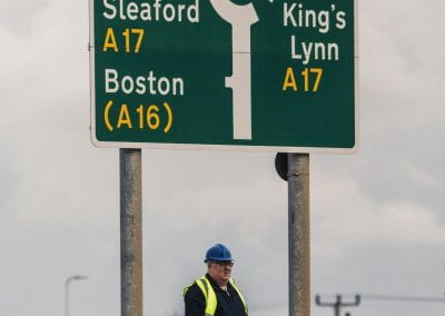 Image of a large roadsign which reads "Peppermint Roundabout" with a man beneath it in a hardhat.