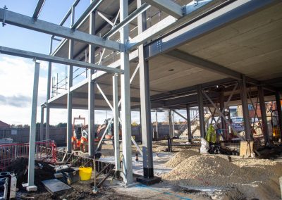 Image of a construction site, a building is in the process of being built, the steel structure is up. Machinery is around it.