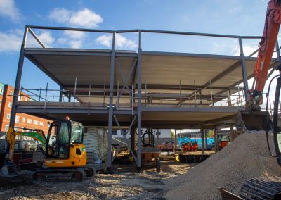 Image of a construction site, a building is in the process of being built, the steel structure is up. Machinery is around it.